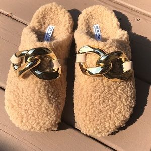 Tan colored house slippers with gold buckles.